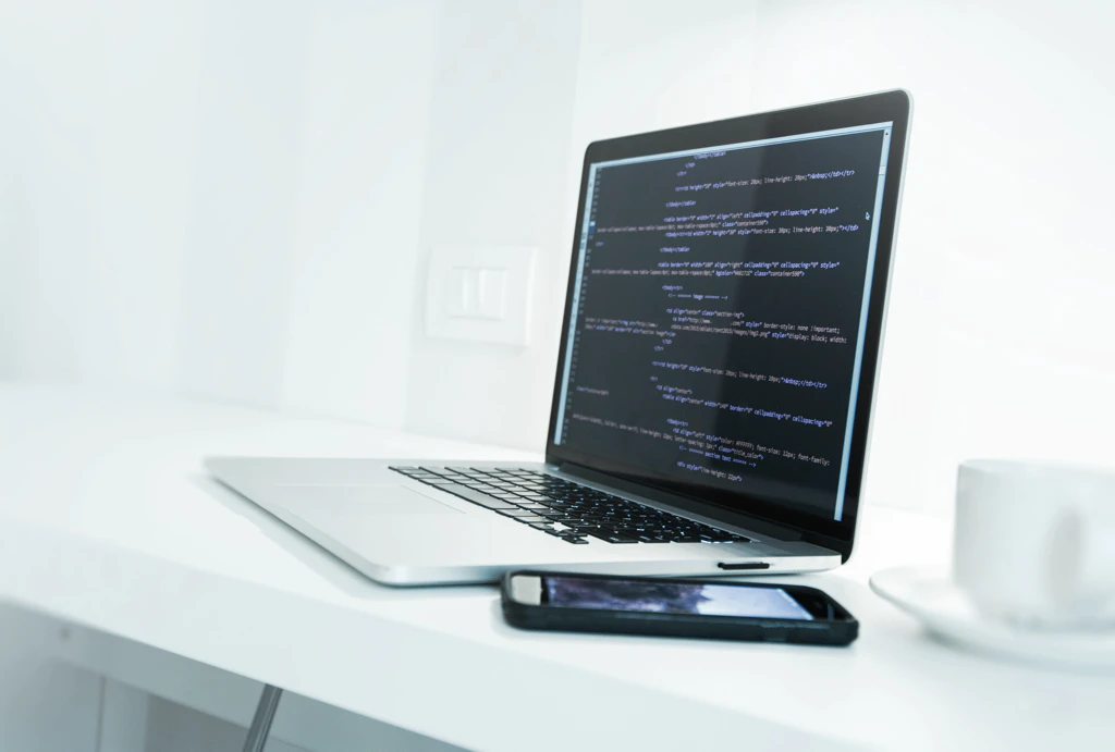 Bild von einem MacBook, neben dem ein Smartphone liegt.